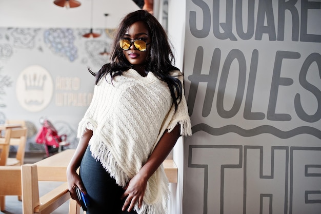 Elegante chica afroamericana con gafas de sol posadas en un café moderno