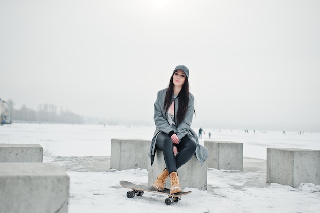 Foto gratuita elegante chica morena con gorra gris estilo casual street con patineta en el día de invierno