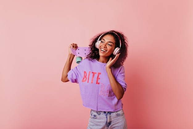 Elegante chica negra de buen humor disfrutando de la música y el baile. Hermosa dama africana rizada divirtiéndose en el estudio.