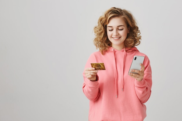 Elegante chica de pelo rizado de compras en línea, con tarjeta de crédito y teléfono inteligente