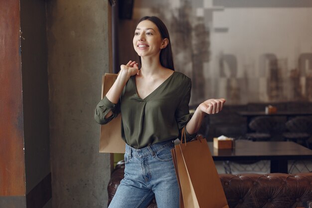 Elegante chica de pie en una cafetería con bolsas de compras