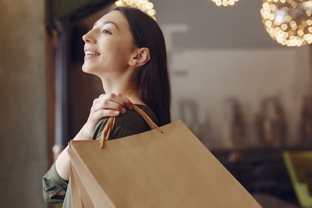 Elegante chica de pie en una cafetería con bolsas de compras