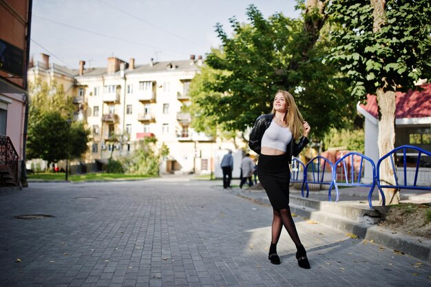 Elegante chica rubia con chaqueta de cuero negro posando en las calles de la ciudad