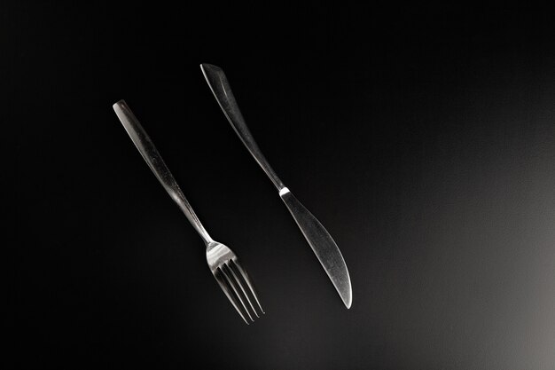 Elegante cuchillo y tenedor de acero inoxidable sobre una mesa negra lisa paralela entre sí frente al espectador