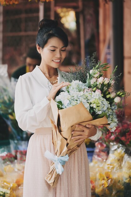 Elegante dama asiática admirando el elaborado ramo de flores frescas en la floristería