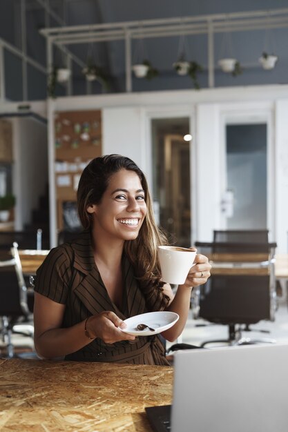 Elegante dama de oficina guapa disfrutando de café caliente sosteniendo la taza sitttin en el café solo
