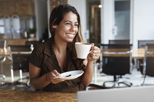 Elegante dama de oficina guapa disfrutando de café caliente sosteniendo la taza sitttin en el café solo