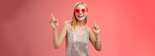 Foto gratuita elegante despreocupada fabulosa joven rubia en vestido plateado gafas de sol rojas divirtiéndose bailando