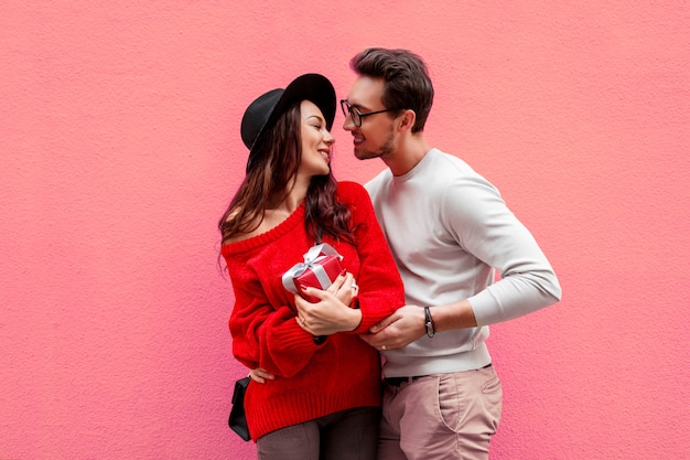 Elegante elegante pareja de enamorados cogidos de la mano y mirándose con placer. Mujer de pelo largo en suéter de punto rojo con su novio posando.