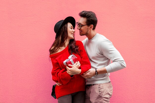 Elegante elegante pareja de enamorados cogidos de la mano y mirándose con placer. Mujer de pelo largo en suéter de punto rojo con su novio posando.