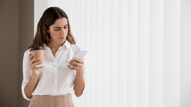 Elegante empresaria con smartphone mientras sostiene la taza de café con espacio de copia