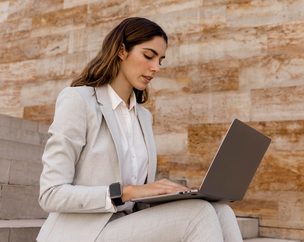 Elegante empresaria con smartwatch trabajando en un portátil al aire libre