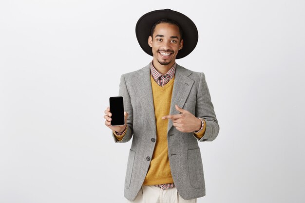 Elegante empresario afroamericano que señala el dedo en la pantalla del teléfono inteligente, mostrando la aplicación