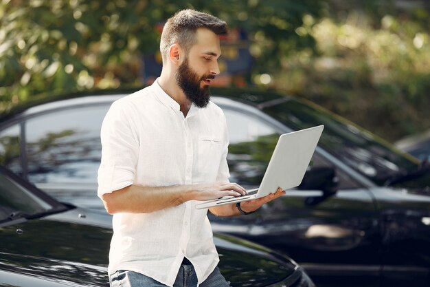 Elegante empresario de pie cerca del coche y usar la computadora portátil