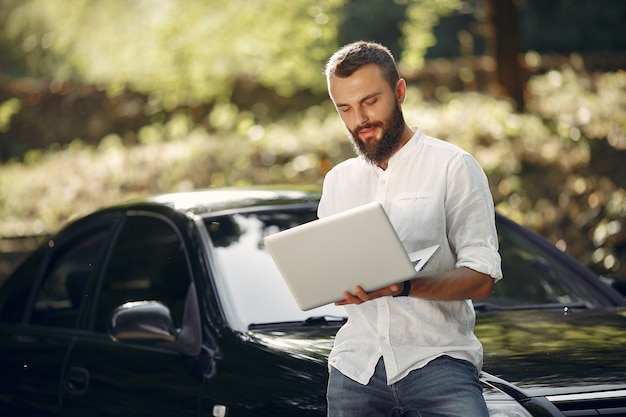 Elegante empresario de pie cerca del coche y usar la computadora portátil