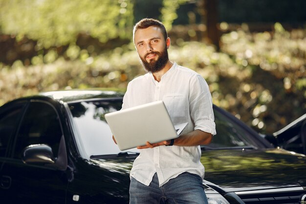 Elegante empresario de pie cerca del coche y usar la computadora portátil