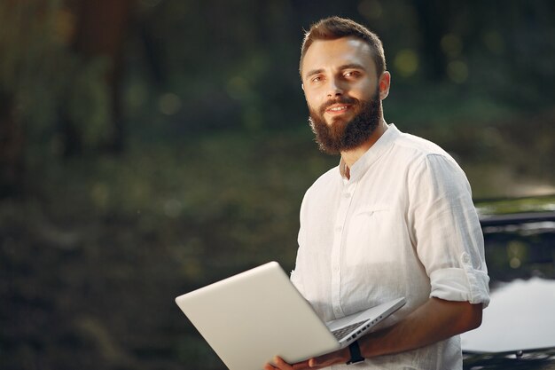 Elegante empresario de pie cerca del coche y usar la computadora portátil