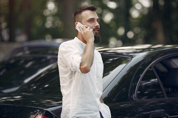 Elegante empresario de pie cerca del coche y usar el teléfono móvil