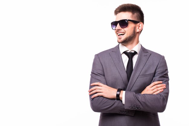 Elegante y encantador. Retrato de joven guapo en ropa formal y gafas de sol ajustando su corbata mientras está de pie contra el fondo gris