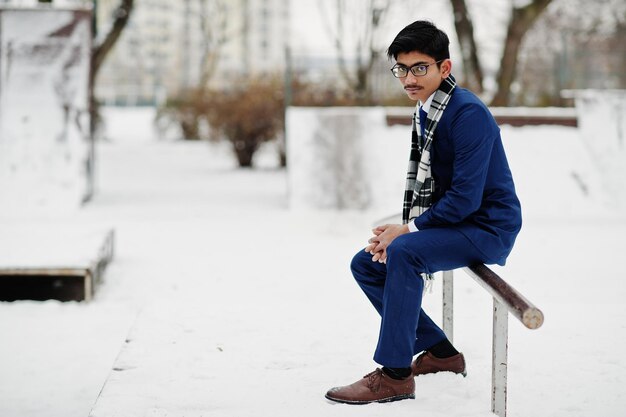 Elegante estudiante indio con gafas de traje y bufanda posado en el día de invierno al aire libre