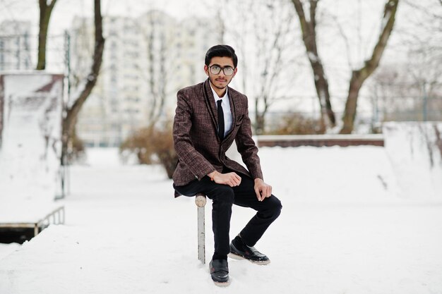 Elegante estudiante indio con traje y gafas posó en el día de invierno al aire libre