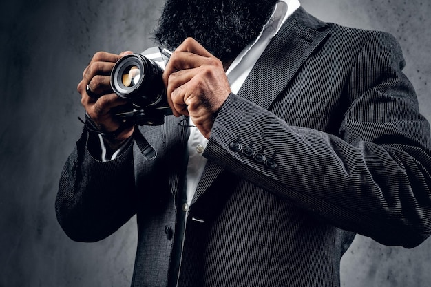 Elegante fotógrafo profesional barbudo en traje de tiro con una cámara réflex digital compacta.