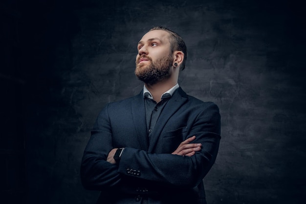 Un elegante hipster barbudo vestido con traje y gafas de sol sobre un fondo gris oscuro.