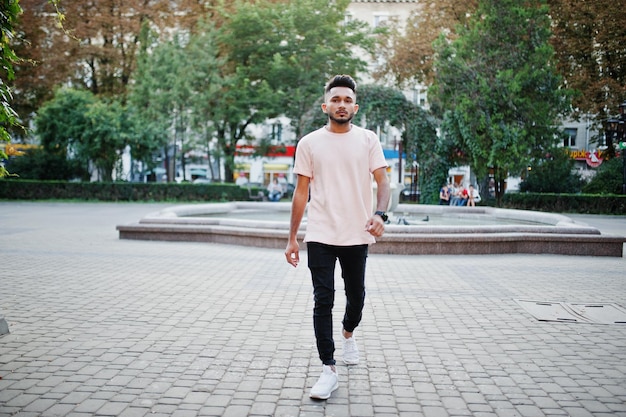 Elegante hombre de barba india con camiseta rosa Modelo de India posado al aire libre en las calles de la ciudad