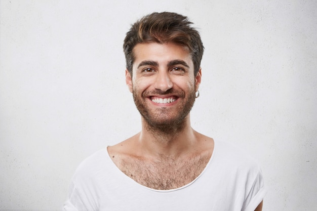 Elegante hombre barbudo con atractivos ojos oscuros sonriendo con expresión complacida de estar contento de conocer a su novia. Chico hipster con barba sonriendo con mirada alegre. Emociones positivas