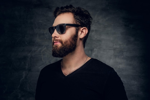 Elegante hombre barbudo con gafas de sol sobre fondo gris.