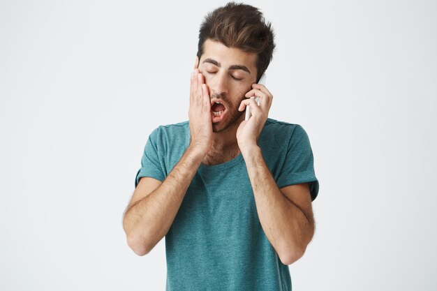 Elegante hombre barbudo con ojos oscuros sonriendo con expresión complacida y contento de hablar con sus padres. Hipster alegre con cara sonriente con teléfono celular. Emociones positivas y comunicación