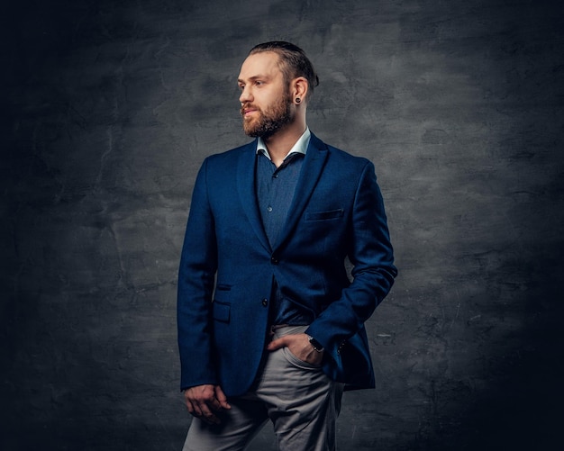 Un elegante hombre barbudo vestido con traje y gafas de sol sobre un fondo gris oscuro.