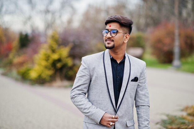 Elegante hombre indio con bindi en la frente y anteojos en traje posado al aire libre