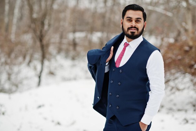 Elegante hombre de negocios de barba india con chaleco y traje posado en el día de invierno al aire libre