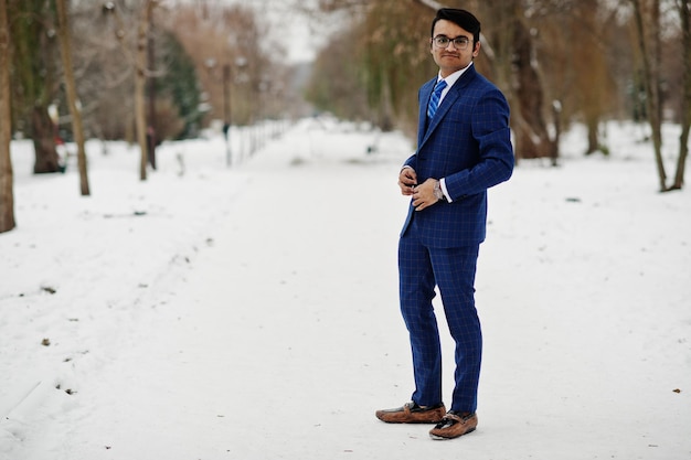 Elegante hombre de negocios indio con traje y gafas posado en el día de invierno al aire libre