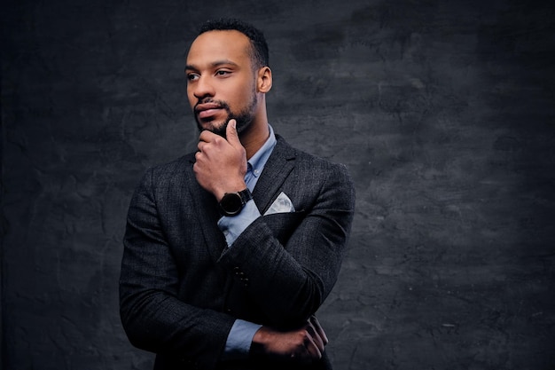 Un elegante hombre negro americano vestido con un traje de fondo gris.