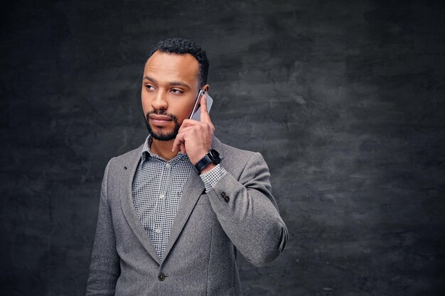 Elegante hombre negro barbudo americano con traje gris habla por teléfono inteligente.