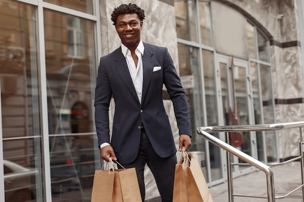 Elegante hombre negro en una ciudad con bolsas de compras