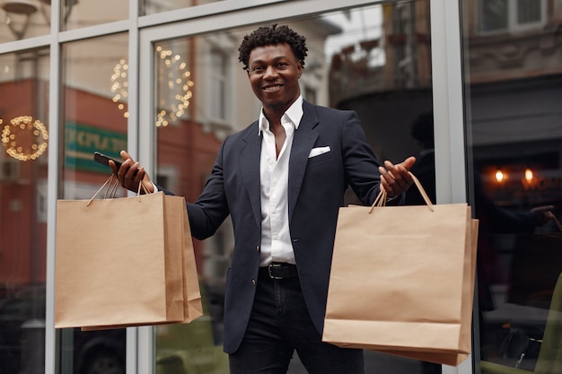 Elegante hombre negro en una ciudad con bolsas de compras