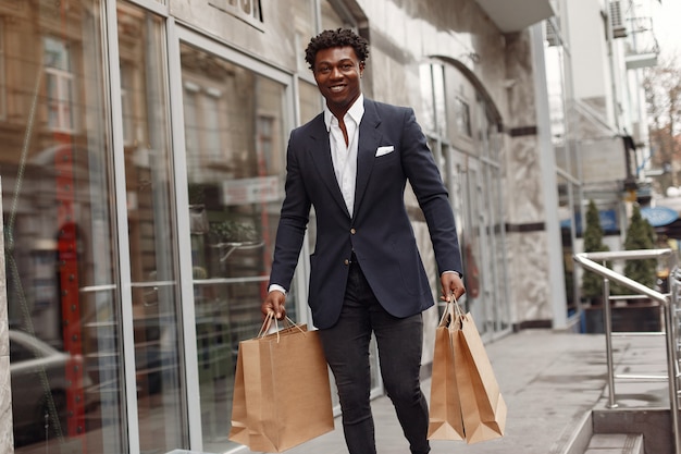 Elegante hombre negro en una ciudad con bolsas de compras