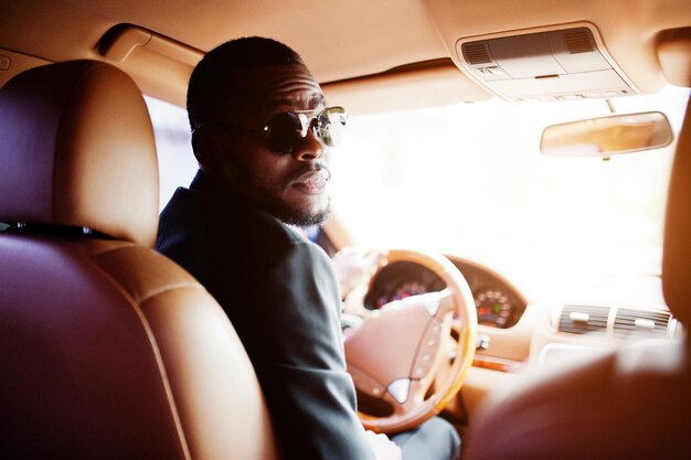 Elegante hombre negro sentado al volante de un auto de lujo Rico hombre de negocios afroamericano