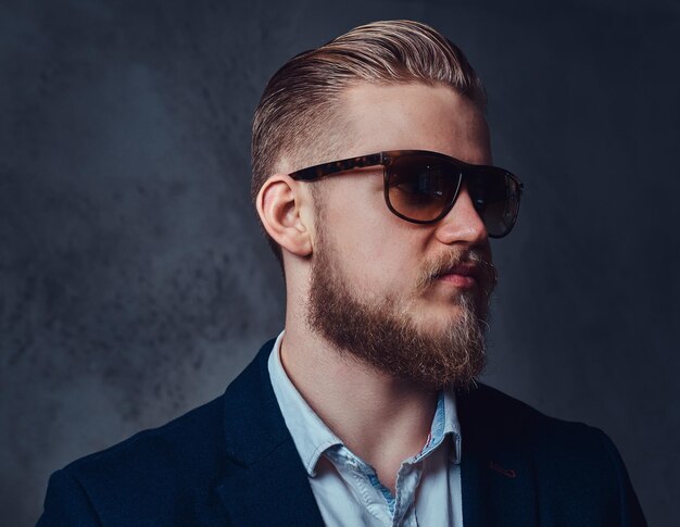 Un elegante hombre rubio con barba vestido con traje y gafas de sol.