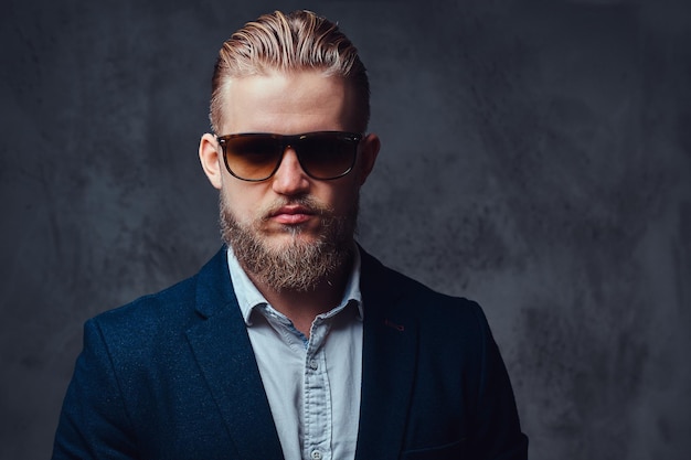 Un elegante hombre rubio con barba vestido con traje y gafas de sol.