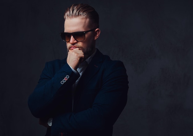 Un elegante hombre rubio con barba vestido con traje y gafas de sol.