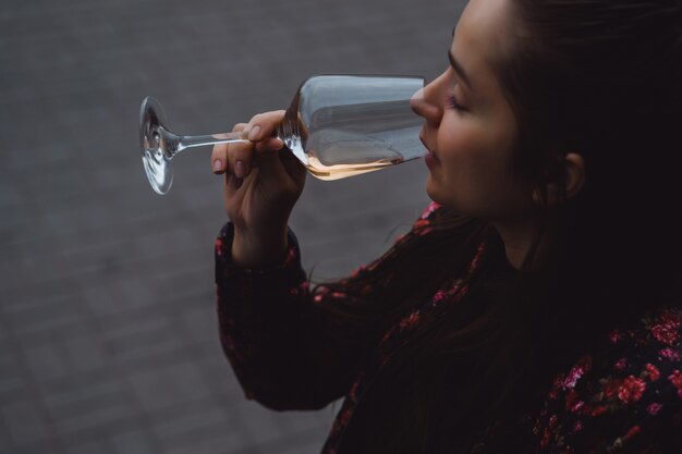 Elegante joven bebe vino en un café de la calle en una terraza de verano. Una muchacha con pelo largo goza de una copa de vino en una tarde del verano. Retrato. de cerca