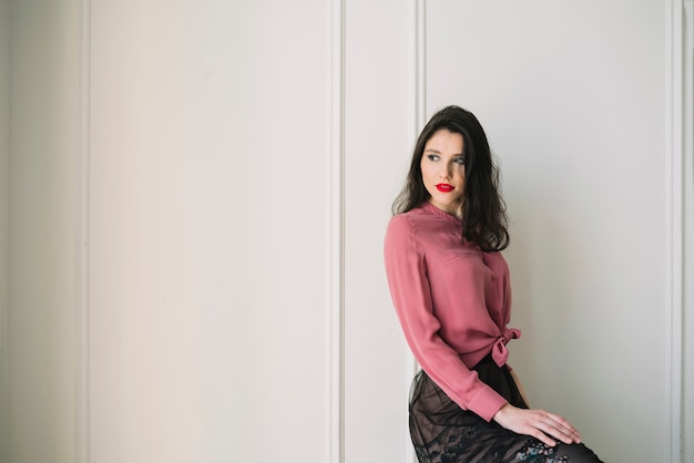 Elegante joven en blusa y falda en habitación.