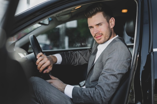 Elegante joven empresario sentado en el coche con una puerta abierta