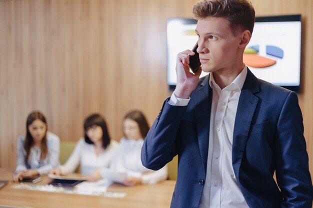 Elegante joven empresario vistiendo una chaqueta y camisa con gente hablando por un teléfono móvil