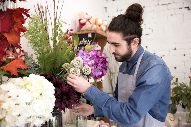 Elegante joven florista masculino arreglando las flores en el ramo