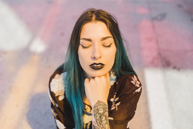 Elegante joven con labio negro y cabello teñido que cierra los ojos.